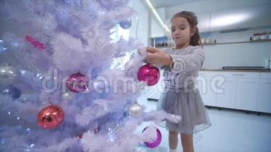 <strong>一个</strong>棕色<strong>小</strong>女孩在家里的一棵人造圣诞树上挂着<strong>一个</strong>粉红色的<strong>玻璃</strong>宝。